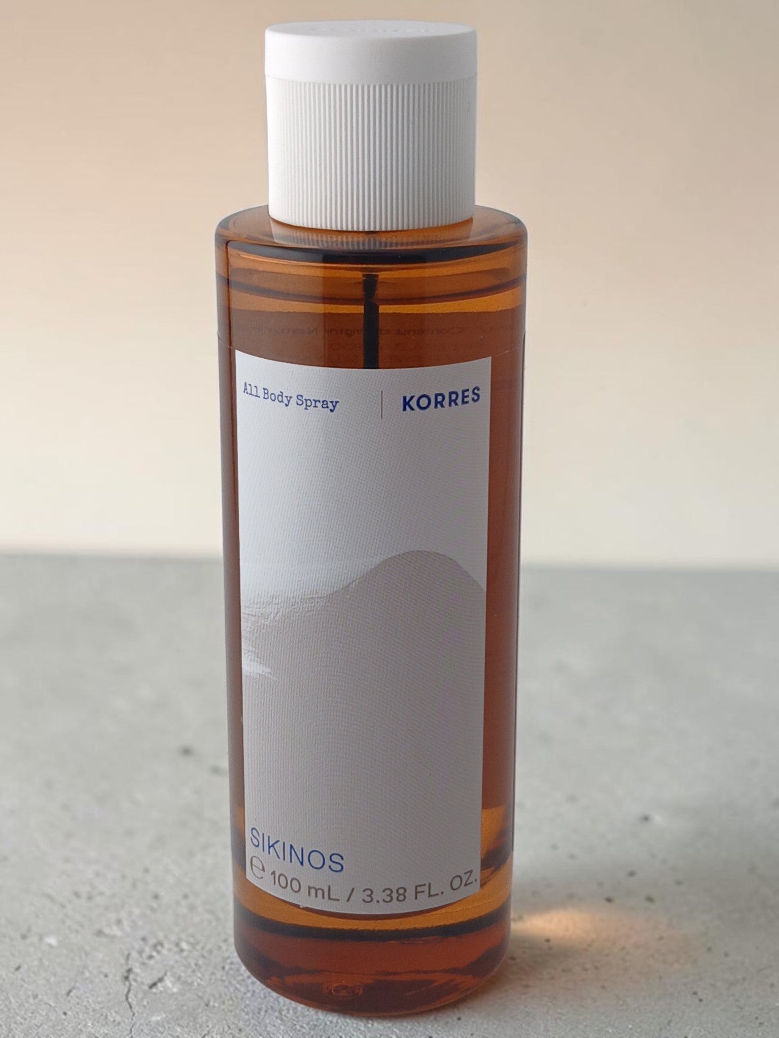 Department Store UK KORRES Sikinos 100ml body spray in a clear amber bottle with a white cap on a neutral surface