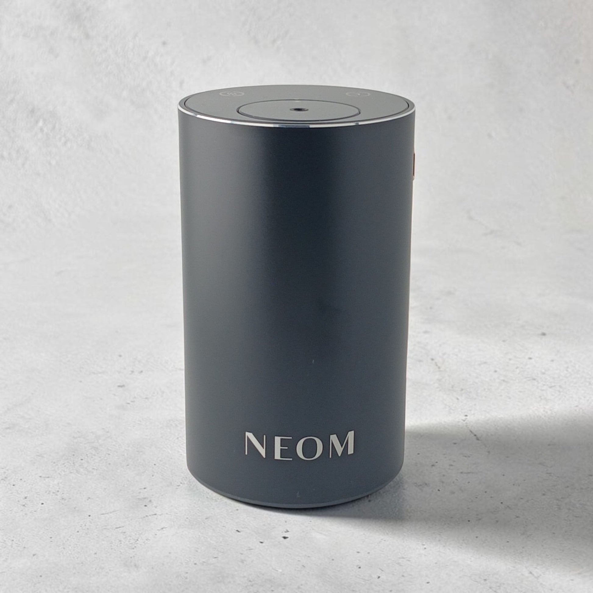 Department Store UK NEOM Wellbeing Pod Mini+ waterless essential oil diffuser in matte black on a wooden table.