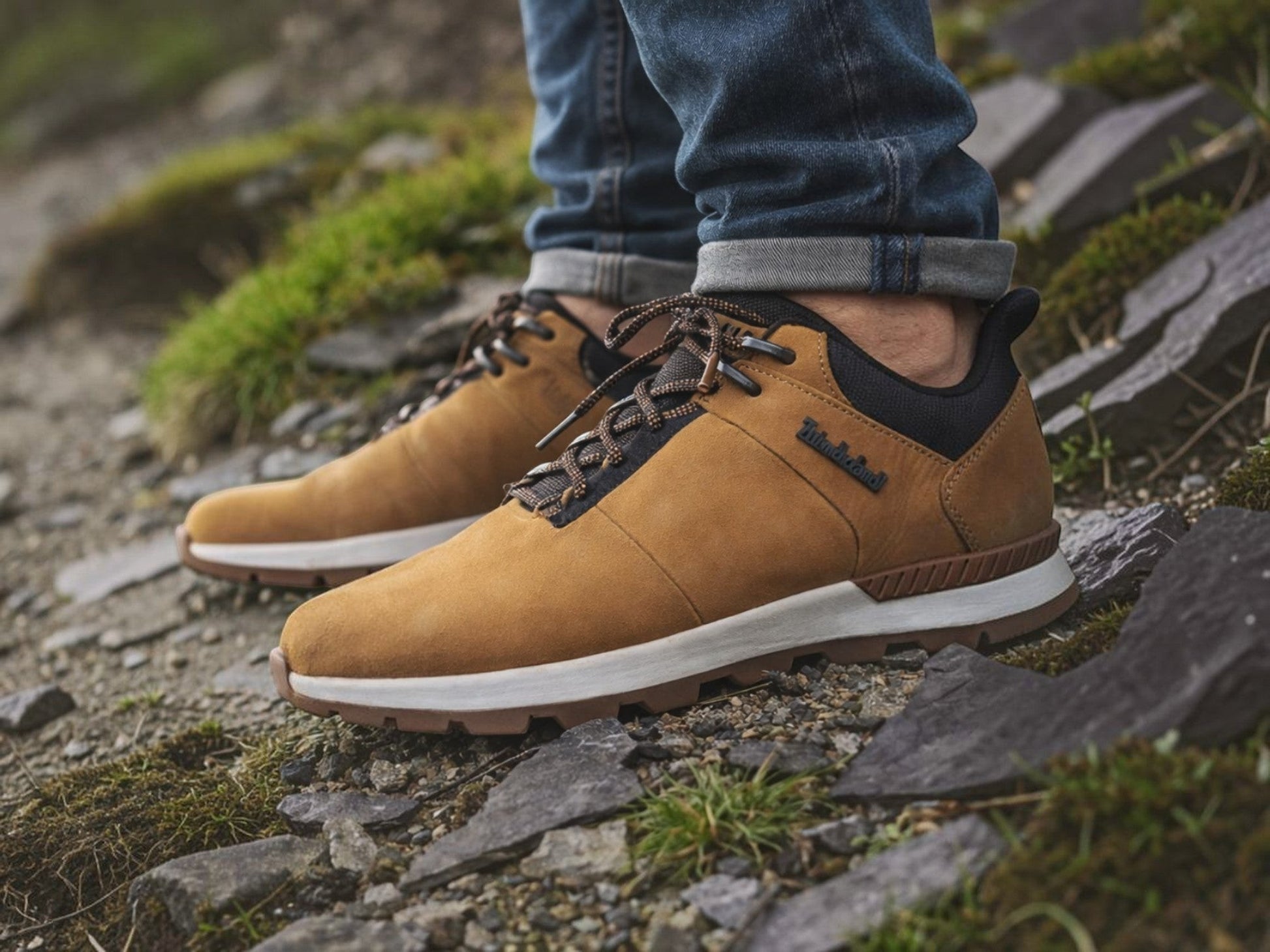 Department Store UK Timberland tan nubuck leather lace-up trainers with black mesh details worn on a stone garden path.